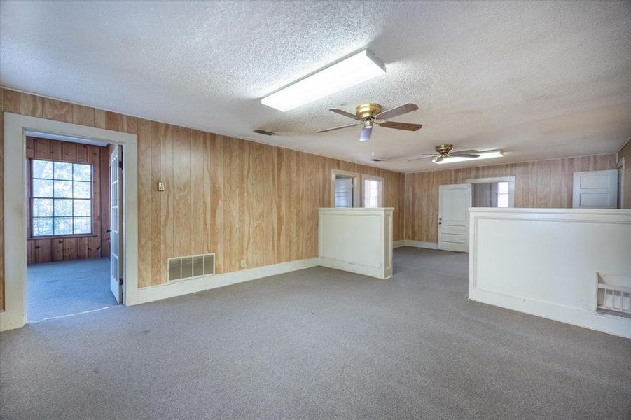 Carpeted empty room with ceiling fan, wood walls, and a textured ceiling