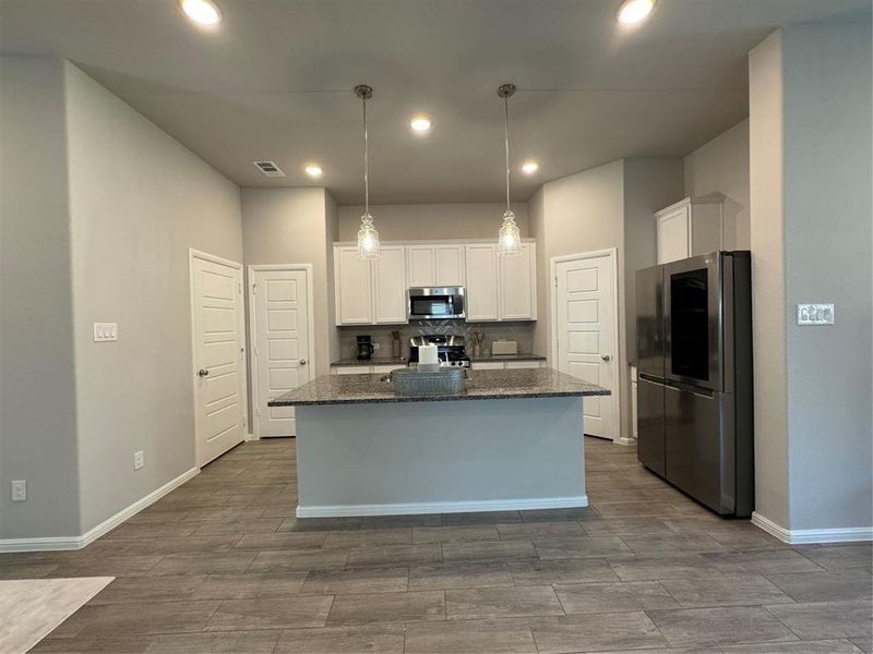 Contemporary kitchen featuring a spacious island with a speckled countertop, white cabinetry, recessed lighting, and wood-finish flooring Contemporary kitchen featuring a spacious island with a speckled countertop, white cabinetry, recessed lighting, and wood-finish flooring