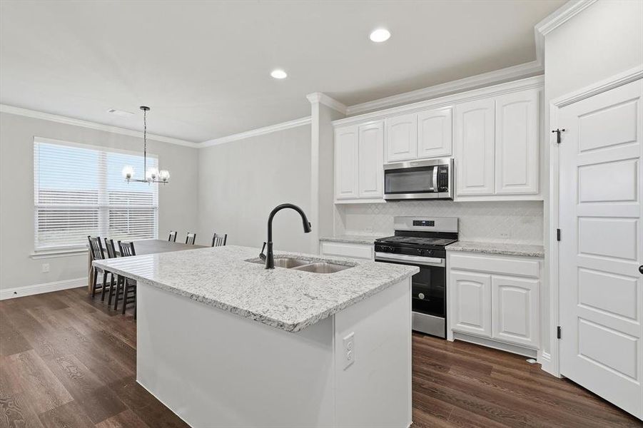 Kitchen with appliances with stainless steel finishes, white cabinetry, light stone counters, hanging light fixtures, and ornamental molding