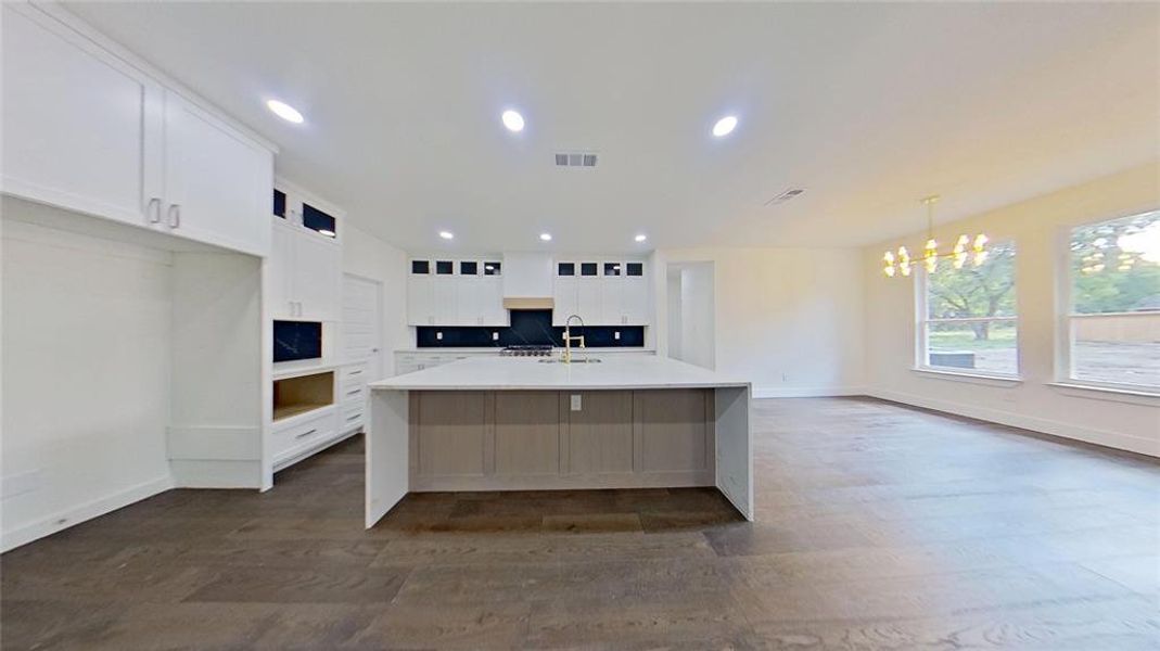 Kitchen featuring white cabinetry, a center island with sink, tasteful backsplash, dark wood-style flooring, and light stone countertops