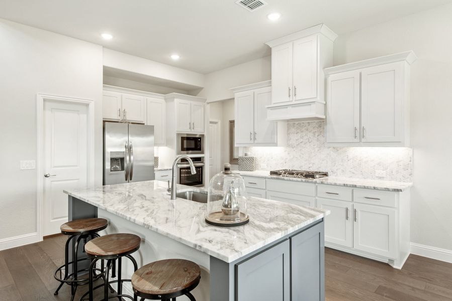 Kitchen with white cabinets, marble island with bar stools, and stainless steel appliances on hardwood floors