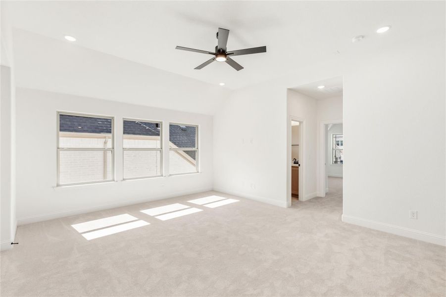 Empty bedroom with light carpet, ceiling fan, three windows, and open doorway to hallway