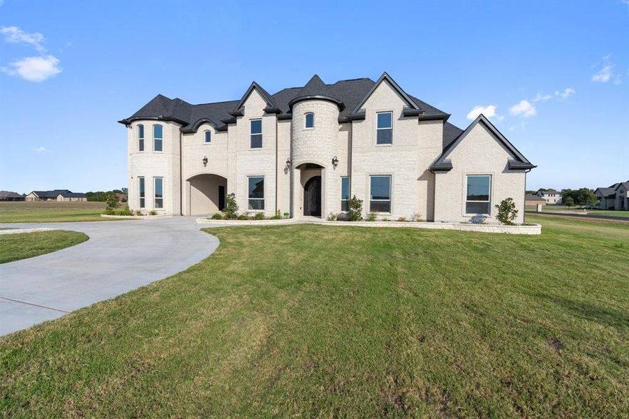 French provincial home with a front yard, concrete driveway, and brick siding