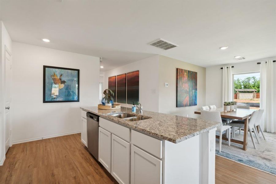 Kitchen featuring white cabinets, stainless steel dishwasher, sink, and light hardwood / wood-style flooring