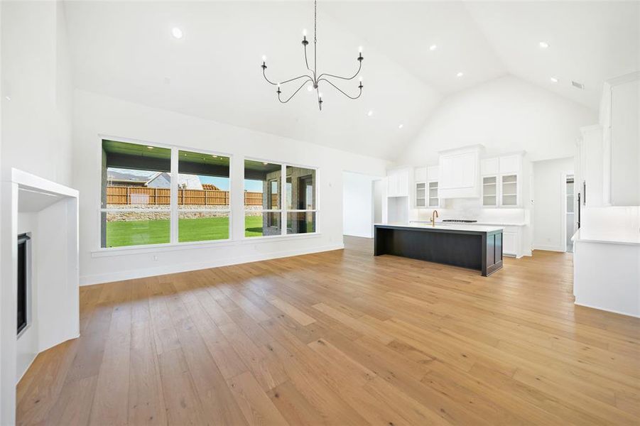 Unfurnished living room with high vaulted ceiling, a chandelier, light wood finished floors, recessed lighting, and a fireplace