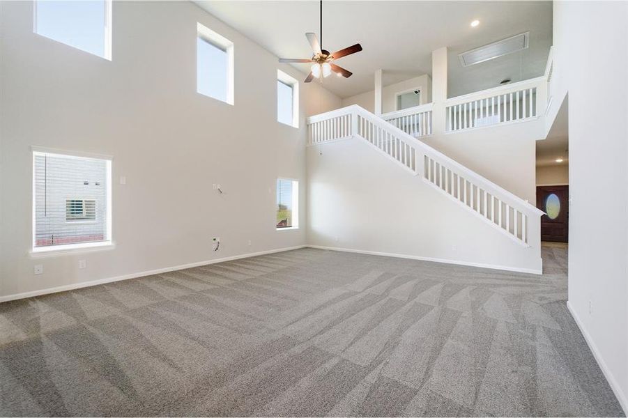 Two-story living area featuring a vaulted ceiling with a ceiling fan, light gray carpet, multiple windows, and a white staircase with balusters leading to an upper landing Two-story living area featuring a vaulted ceiling with a ceiling fan, light gray carpet, multiple windows, and a white staircase with balusters leading to an upper landing