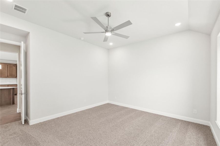 Empty bedroom with beige carpet, white walls, and a modern ceiling fan with light fixture.