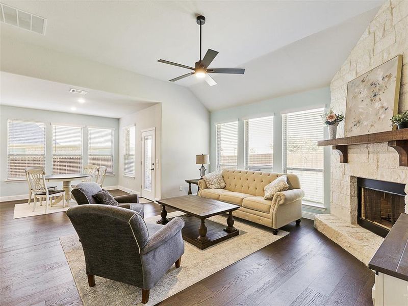 Living room with a stone fireplace, lofted ceiling, plenty of natural light, and dark hardwood / wood-style flooring