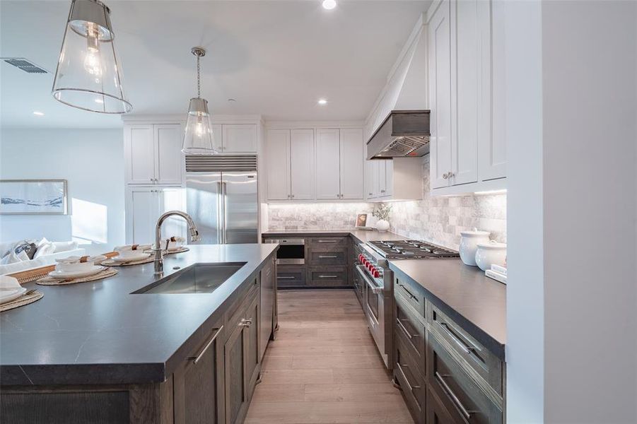 Kitchen featuring sink, white cabinetry, a kitchen island with sink, hanging light fixtures, and high end appliances