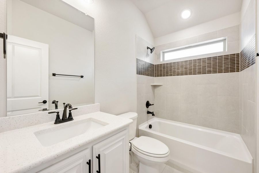Bathroom with white vanity, quartz countertop, tub-shower combo with brown tile accent strip, and black hardware fixtures.
