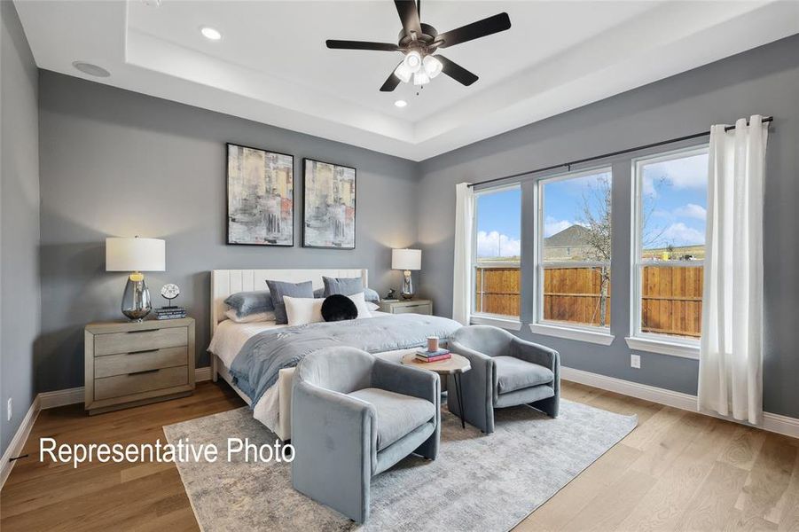 Spacious bedroom featuring light wood-finish flooring, a tray ceiling with recessed lighting, and a ceiling fan