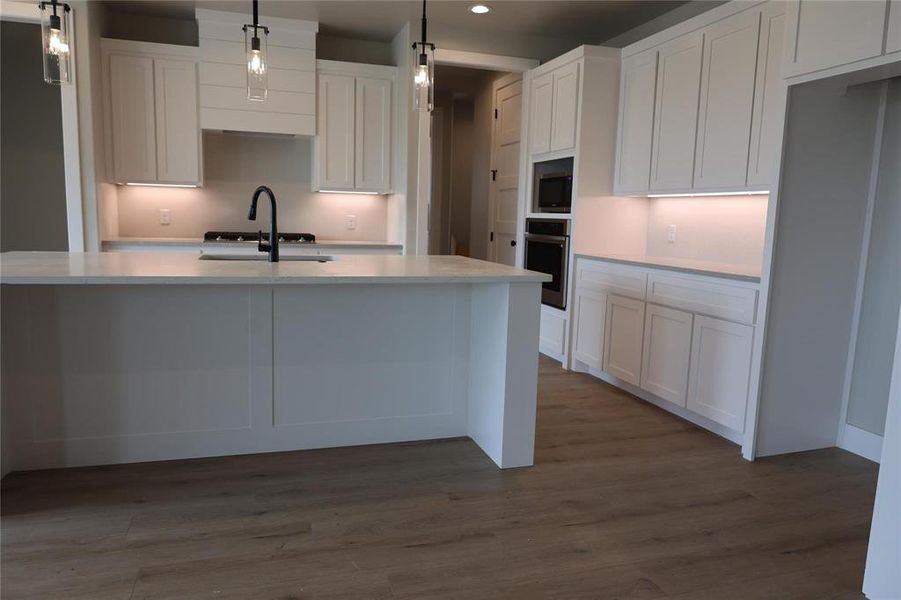 Kitchen with stainless steel appliances, sink, an island with sink, white cabinetry, and dark wood-type flooring