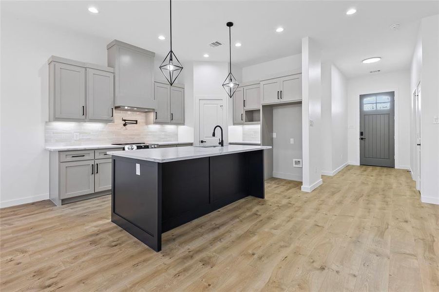 Kitchen with visible vents, premium range hood, a sink, light countertops, and backsplash