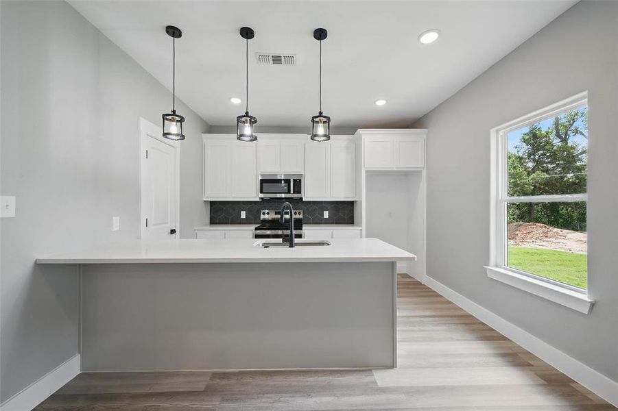 Kitchen featuring appliances with stainless steel finishes, tasteful backsplash, light countertops, a sink, and white cabinets
