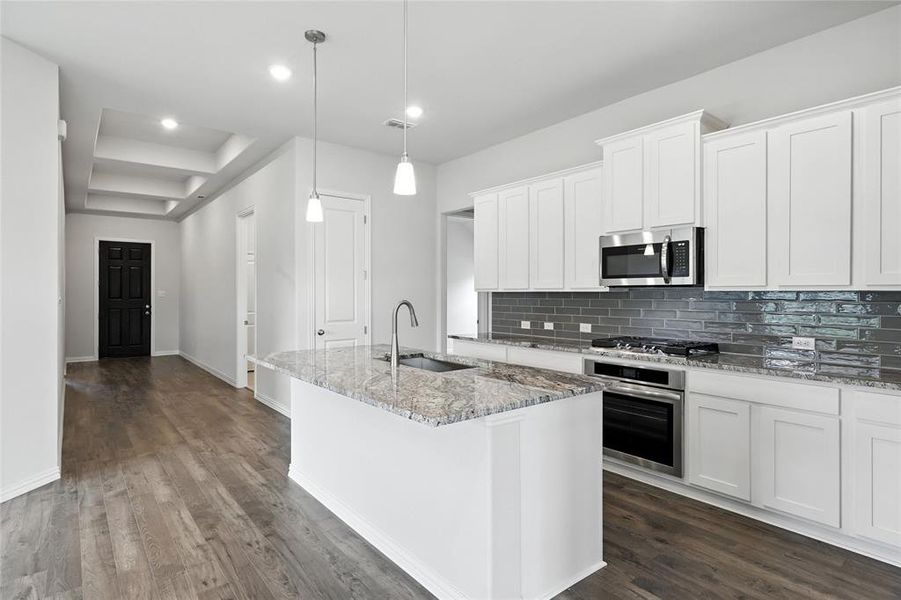 Kitchen featuring appliances with stainless steel finishes, tasteful backsplash, a kitchen island with sink, dark wood finished floors, and recessed lighting