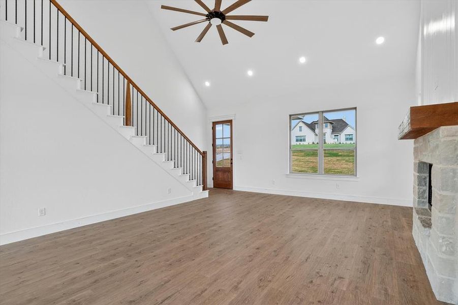 Spacious living area featuring wood-finish flooring, a stone fireplace with a wood mantel, a high vaulted ceiling with a ceiling fan, and recessed lighting