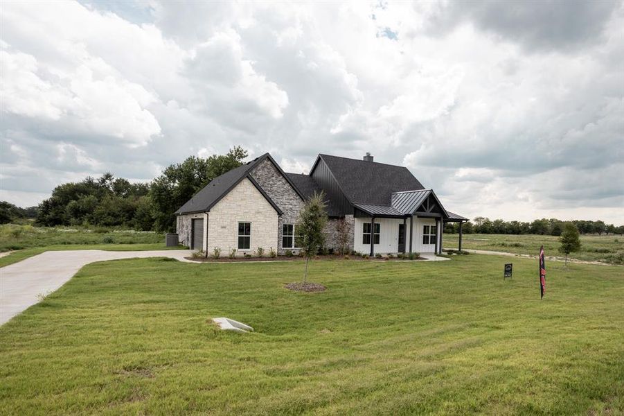View of front of home featuring driveway, stone siding, a standing seam roof, a front lawn, and a porch View of front of home featuring driveway, stone siding, a standing seam roof, a front lawn, and a porch