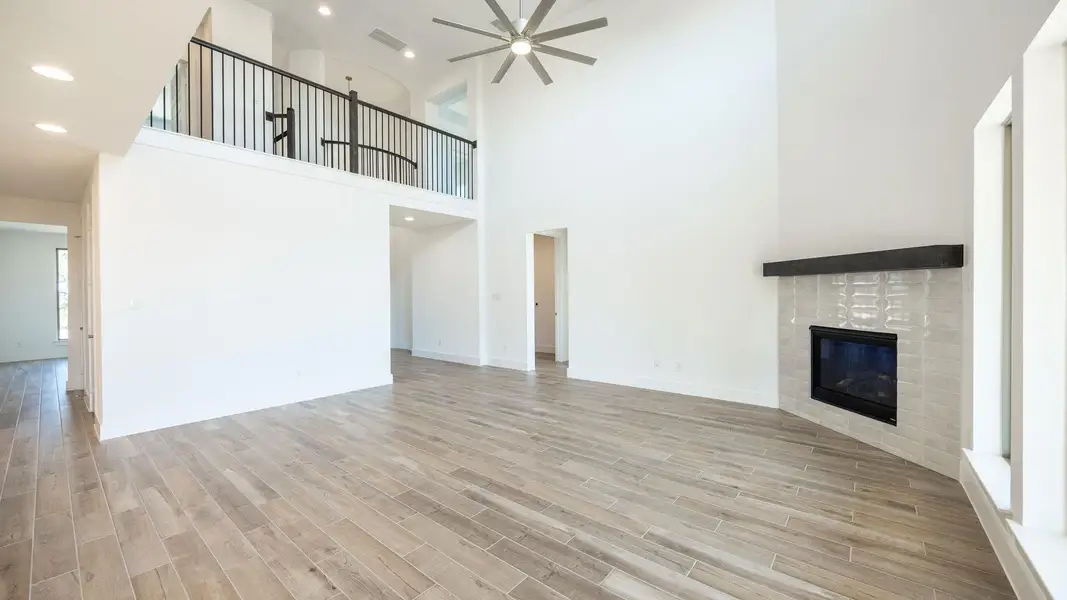 Unfurnished living room featuring a tiled fireplace, light wood finished floors, recessed lighting, a towering ceiling, and a ceiling fan Unfurnished living room featuring a tiled fireplace, light wood finished floors, recessed lighting, a towering ceiling, and a ceiling fan