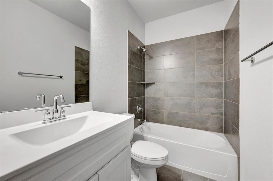Bathroom featuring a single white vanity with a rectangular sink and chrome faucet, a large wall-mounted mirror, a tub/shower combination with large format gray tile surround, an integrated shower shelf, and a chrome towel bar