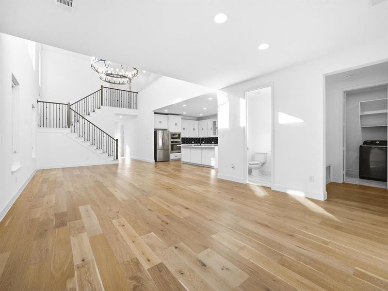 Unfurnished living room featuring stairway, light wood-style floors, recessed lighting, washer / clothes dryer, and a chandelier Unfurnished living room featuring stairway, light wood-style floors, recessed lighting, washer / clothes dryer, and a chandelier