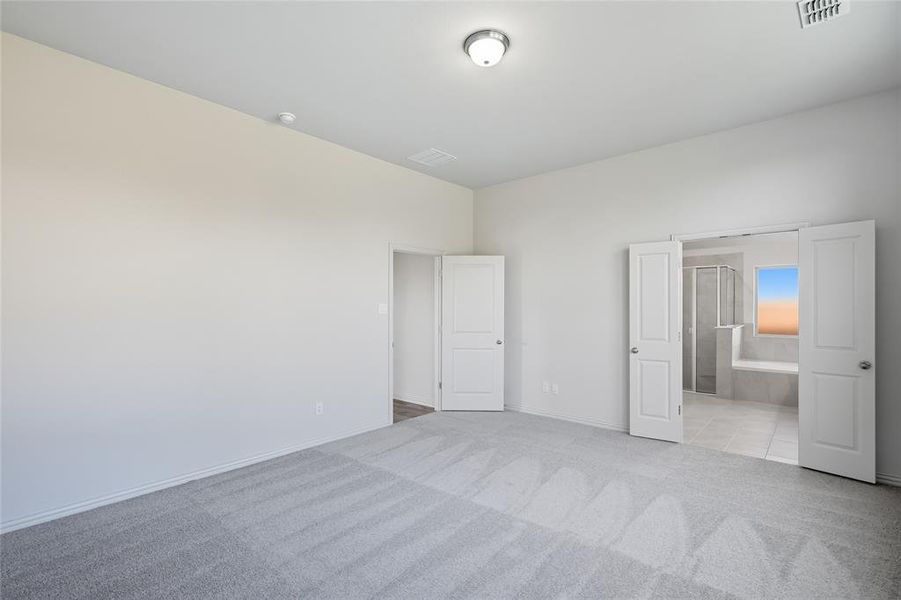 Unfurnished bedroom with light colored carpet, connected bathroom, and light tile patterned floors Unfurnished bedroom with light colored carpet, connected bathroom, and light tile patterned floors