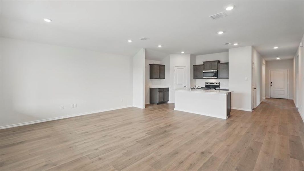 Open-concept living area featuring wood-finish flooring, recessed lighting, and a kitchen with dark cabinetry, stainless steel appliances, and a central island with a white countertop