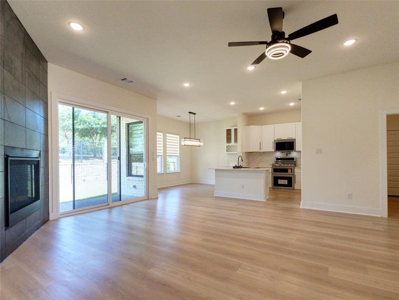 Open-concept living space featuring wood-finish flooring, a contemporary fireplace with tile surround, and a modern ceiling fan
