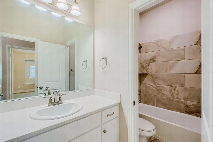 Full bathroom featuring vanity, tiled shower / bath combo, and toilet