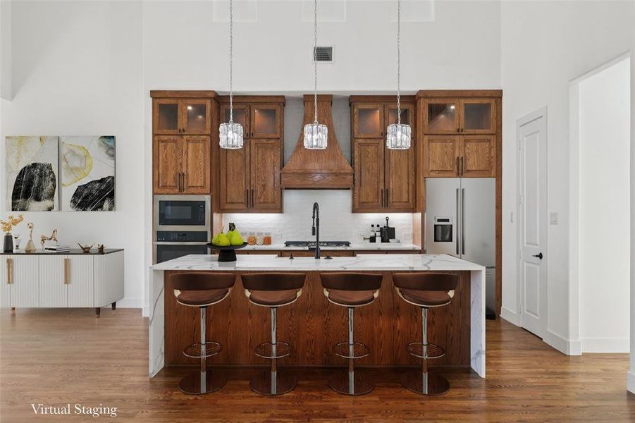 Kitchen with brown cabinetry, a kitchen breakfast bar, light stone counters, hanging light fixtures, and stainless steel appliances