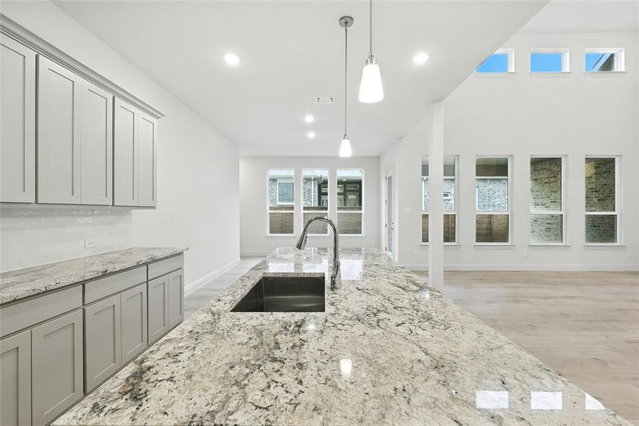 Kitchen with light stone counters, gray cabinetry, pendant lighting, light wood-style flooring, and recessed lighting