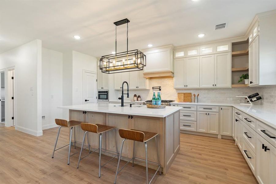 Kitchen featuring open shelves, hanging light fixtures, glass insert cabinets, decorative backsplash, and a breakfast bar area Kitchen featuring open shelves, hanging light fixtures, glass insert cabinets, decorative backsplash, and a breakfast bar area