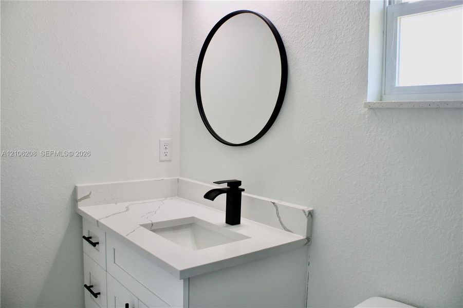 White vanity featuring a stone-look countertop, integrated rectangular sink, matte black faucet, and circular wall-mounted mirror