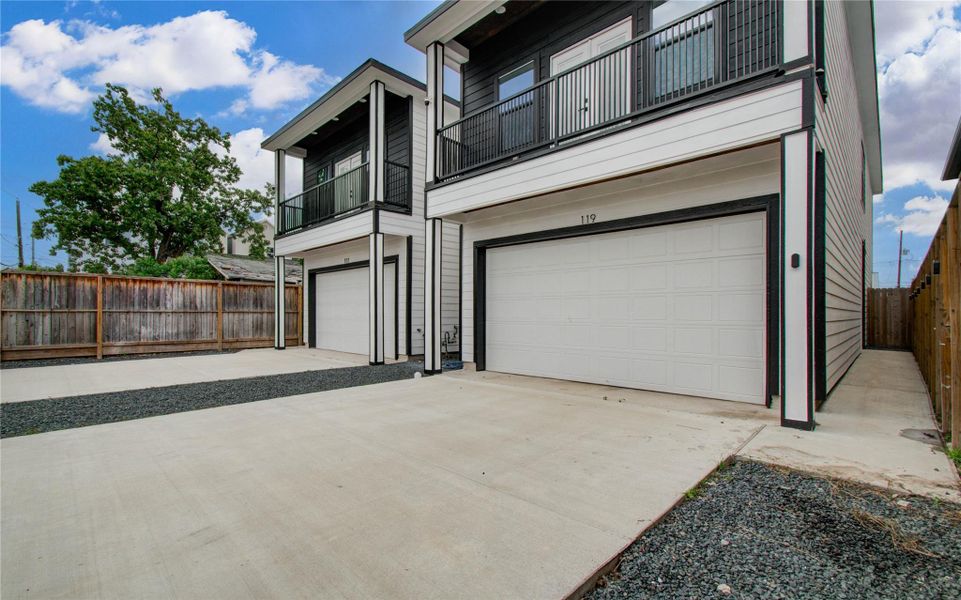 Clean exterior, featuring a double garage and a spacious driveway. The upper level includes a balcony, and the property is enclosed with wooden fencing, providing privacy.