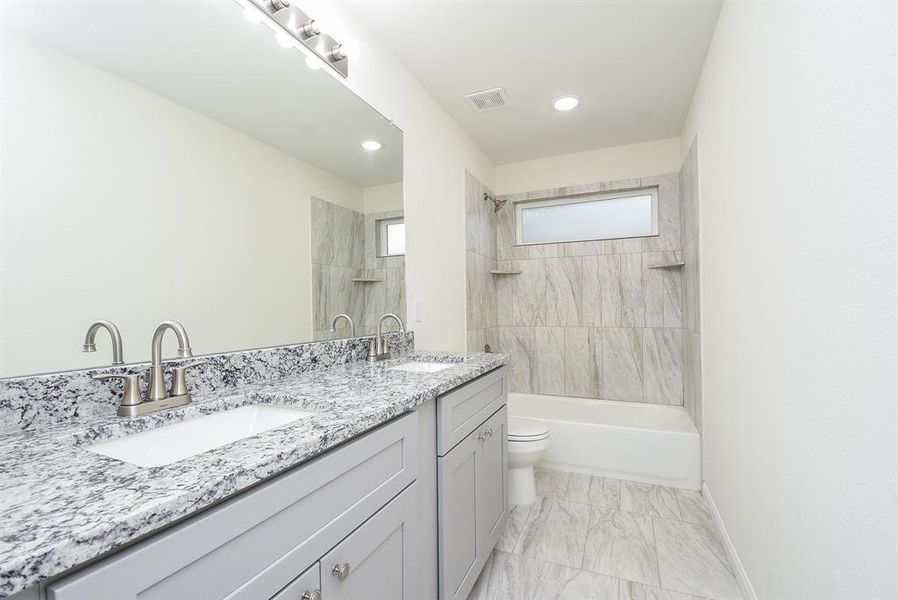 Modern bathroom with double vanity, large mirror, marble countertops, tiled walls, and a bathtub with overhead lighting.