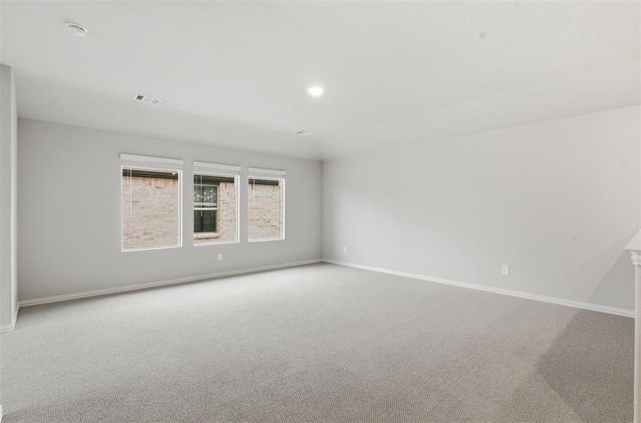 Spacious interior room with light grey walls, grey carpet, and three windows providing natural light