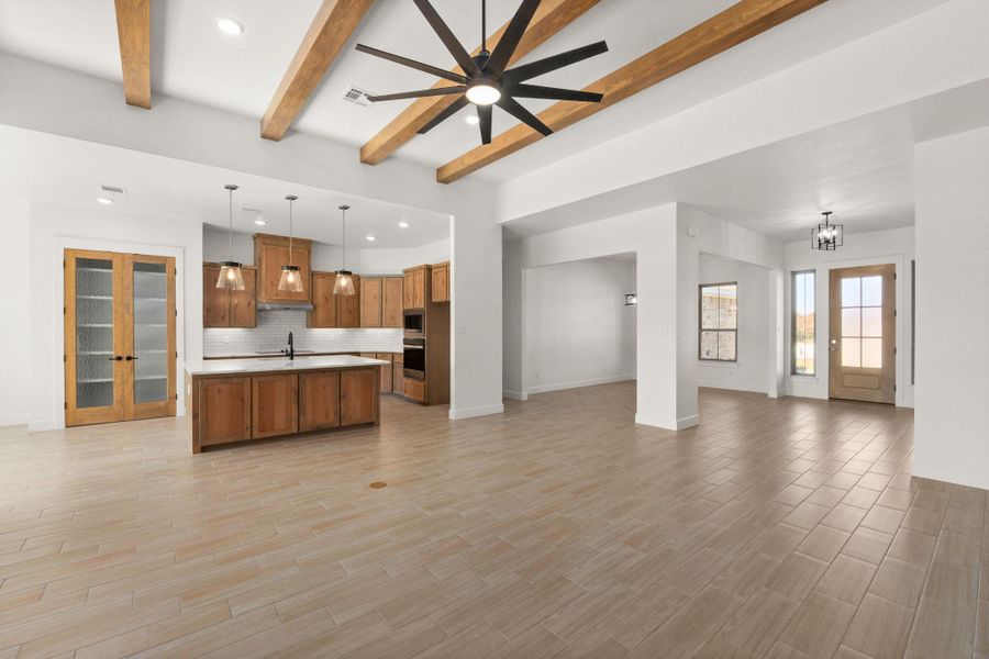 Unfurnished living room featuring recessed lighting, beamed ceiling, ceiling fan, light wood finished floors, and a chandelier