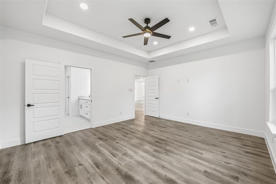 Unfurnished bedroom with a tray ceiling, ceiling fan, light wood-type flooring, connected bathroom, and recessed lighting