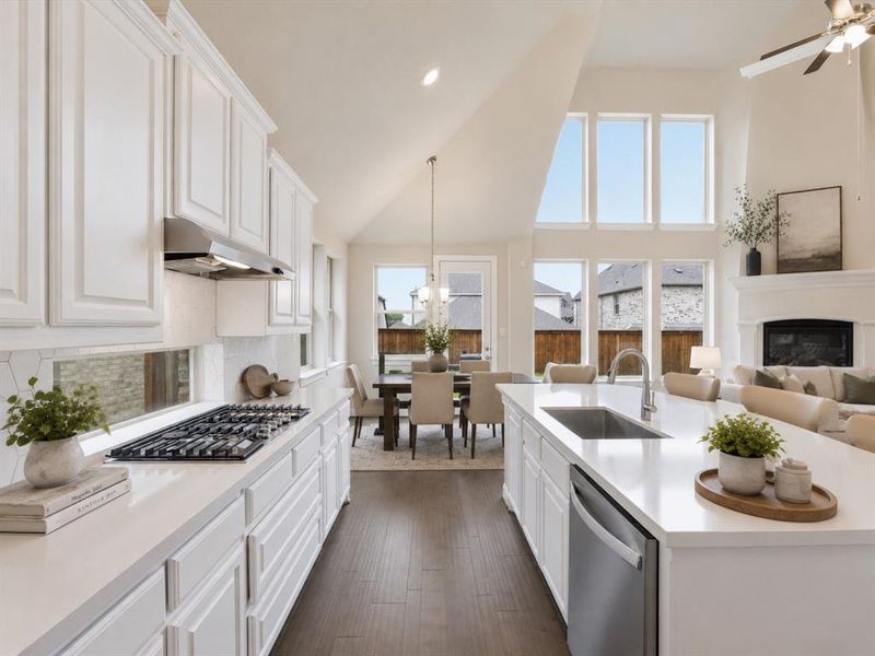 Open-concept kitchen featuring white cabinetry, light-toned countertops, a built-in gas cooktop with stainless steel hood, and a kitchen island with an undermount sink and integrated dishwasher