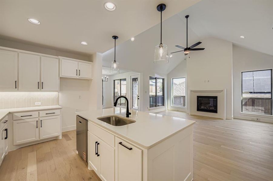 Kitchen featuring a center island with sink, a high ceiling, a glass covered fireplace, light wood-type flooring, and open floor plan