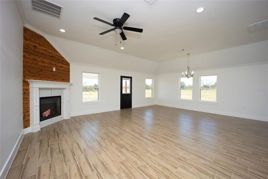 Unfurnished living room with vaulted ceiling, healthy amount of natural light, a fireplace, wood tiled floors, and ceiling fan