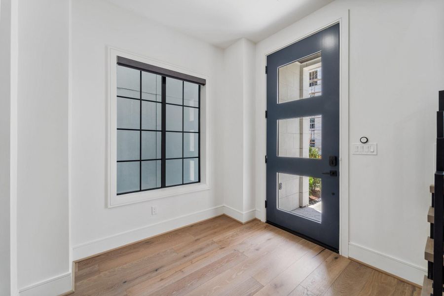 A striking blue entry door with glass panels welcomes you inside, where light wood flooring and a black-framed picture window create a bright, sophisticated first impression. A striking blue entry door with glass panels welcomes you inside, where light wood flooring and a black-framed picture window create a bright, sophisticated first impression.