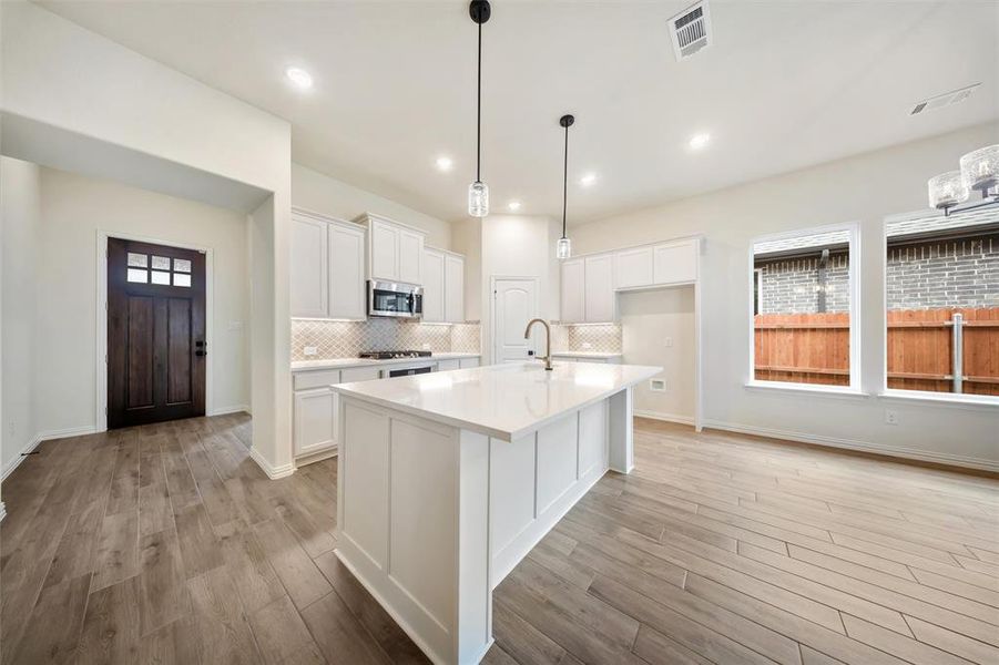Kitchen with light wood-type flooring, white cabinets, decorative backsplash, light countertops, and a kitchen island with sink
