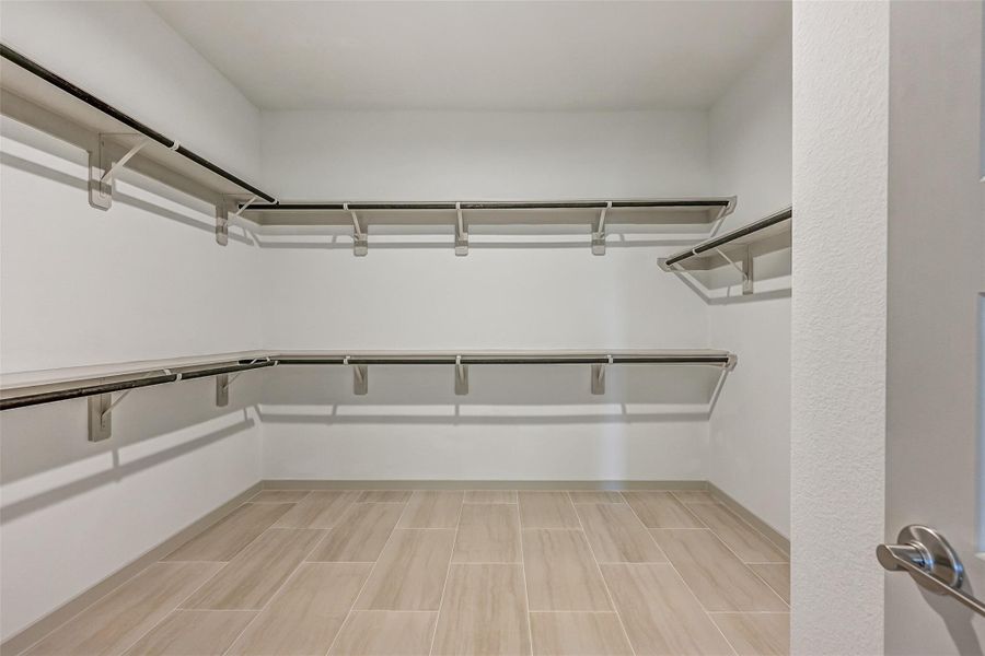 The generous primary walk-in closet provides extensive double-tier hanging and shelf space on multiple walls, along with easy-care tile flooring for exceptional storage and organization. The generous primary walk-in closet provides extensive double-tier hanging and shelf space on multiple walls, along with easy-care tile flooring for exceptional storage and organization.