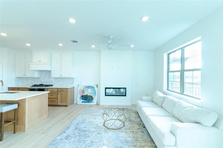 Living room with a glass covered fireplace, light wood finished floors, ceiling fan, and recessed lighting