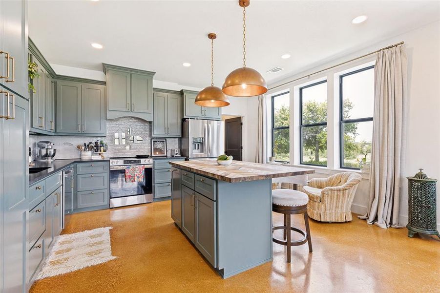 Spacious kitchen featuring sage cabinetry, stainless steel appliances, a center island with seating, and ample natural light from multiple windows Spacious kitchen featuring sage cabinetry, stainless steel appliances, a center island with seating, and ample natural light from multiple windows