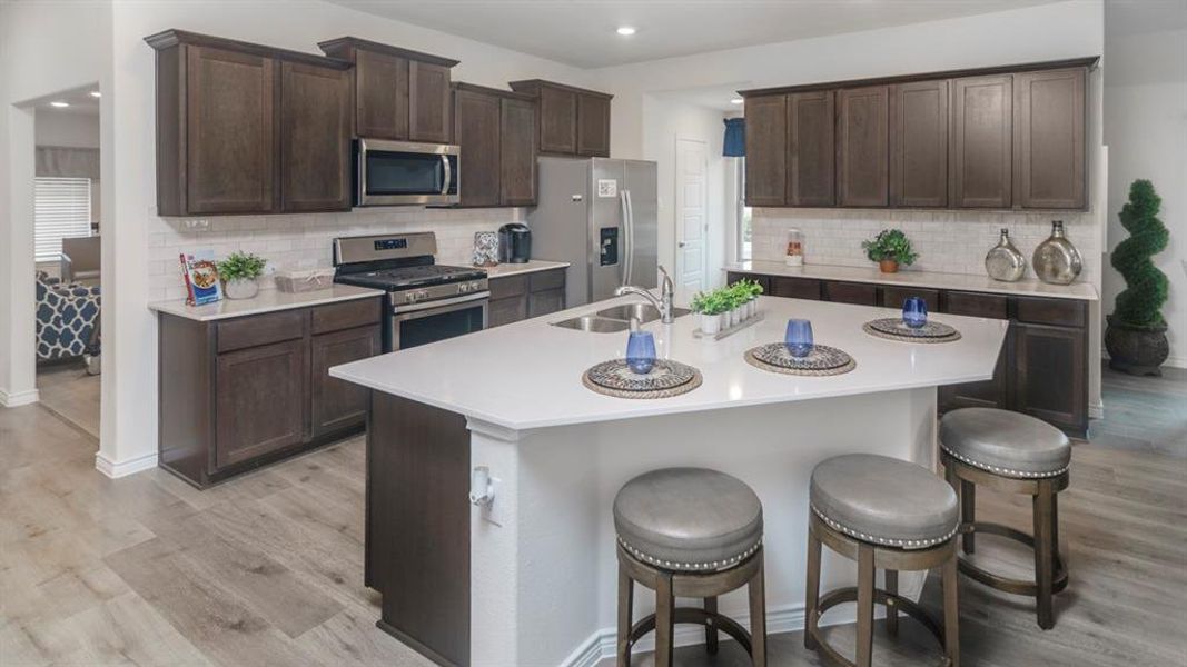 Kitchen featuring a central island with countertop seating, wood-finish flooring, dark wood cabinetry, white subway tile backsplash, and stainless steel appliances