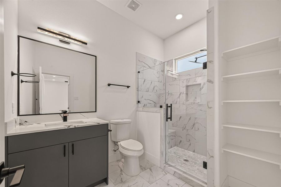 This modern bathroom features a sleek design with a spacious glass-enclosed shower, marble-style tiles, a large mirror, and ample shelving for storage. This modern bathroom features a sleek design with a spacious glass-enclosed shower, marble-style tiles, a large mirror, and ample shelving for storage.