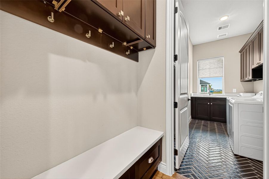 Practical built-ins and coat hooks offer everyday convenience near the garage entry. The laundry room features elegant herringbone tile flooring, abundant cabinetry, and a window overlooking the lake. Practical built-ins and coat hooks offer everyday convenience near the garage entry. The laundry room features elegant herringbone tile flooring, abundant cabinetry, and a window overlooking the lake.