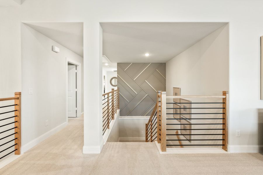 Upper hallway with wood and metal railings, carpeted floors, and a herringbone accent wall at the staircase landing