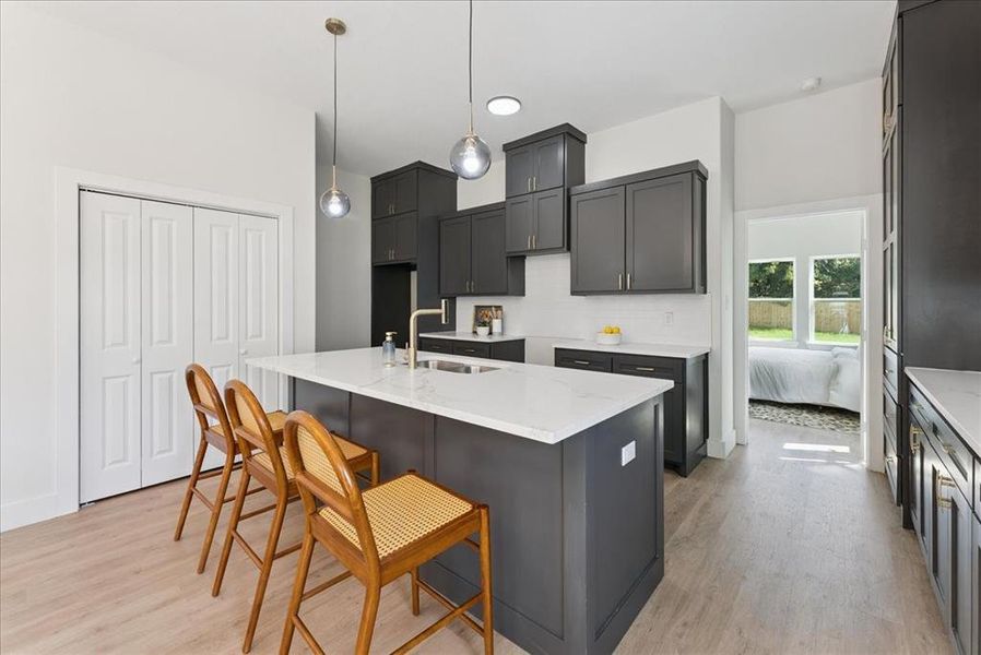 Kitchen with a kitchen island with sink, decorative backsplash, light stone countertops, a kitchen breakfast bar, and light wood-type flooring